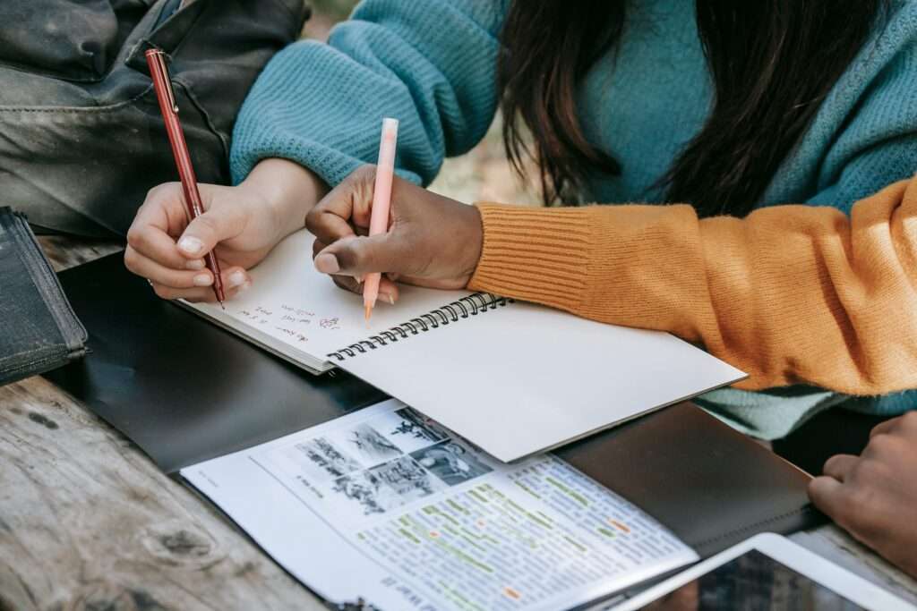 Two students studying together outdoors, writing notes and collaborating on a project.